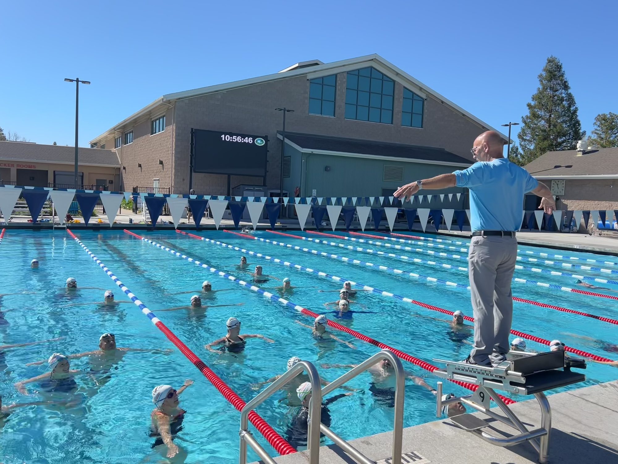 Bill Brenner on a starting block demonstrates arm position to swimmers in an outdoor pool