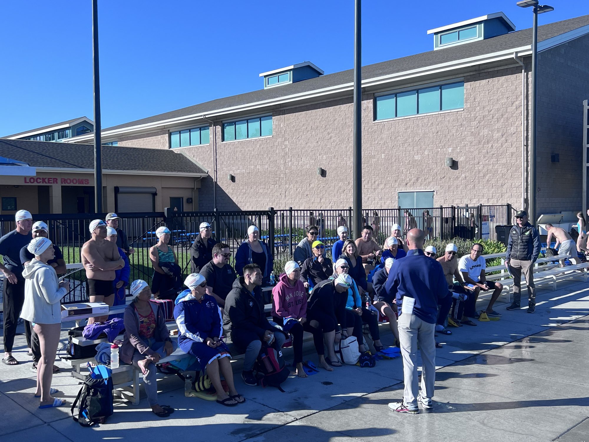 Adult swimmers seated on deck listen to Bill Brenner before a clinic