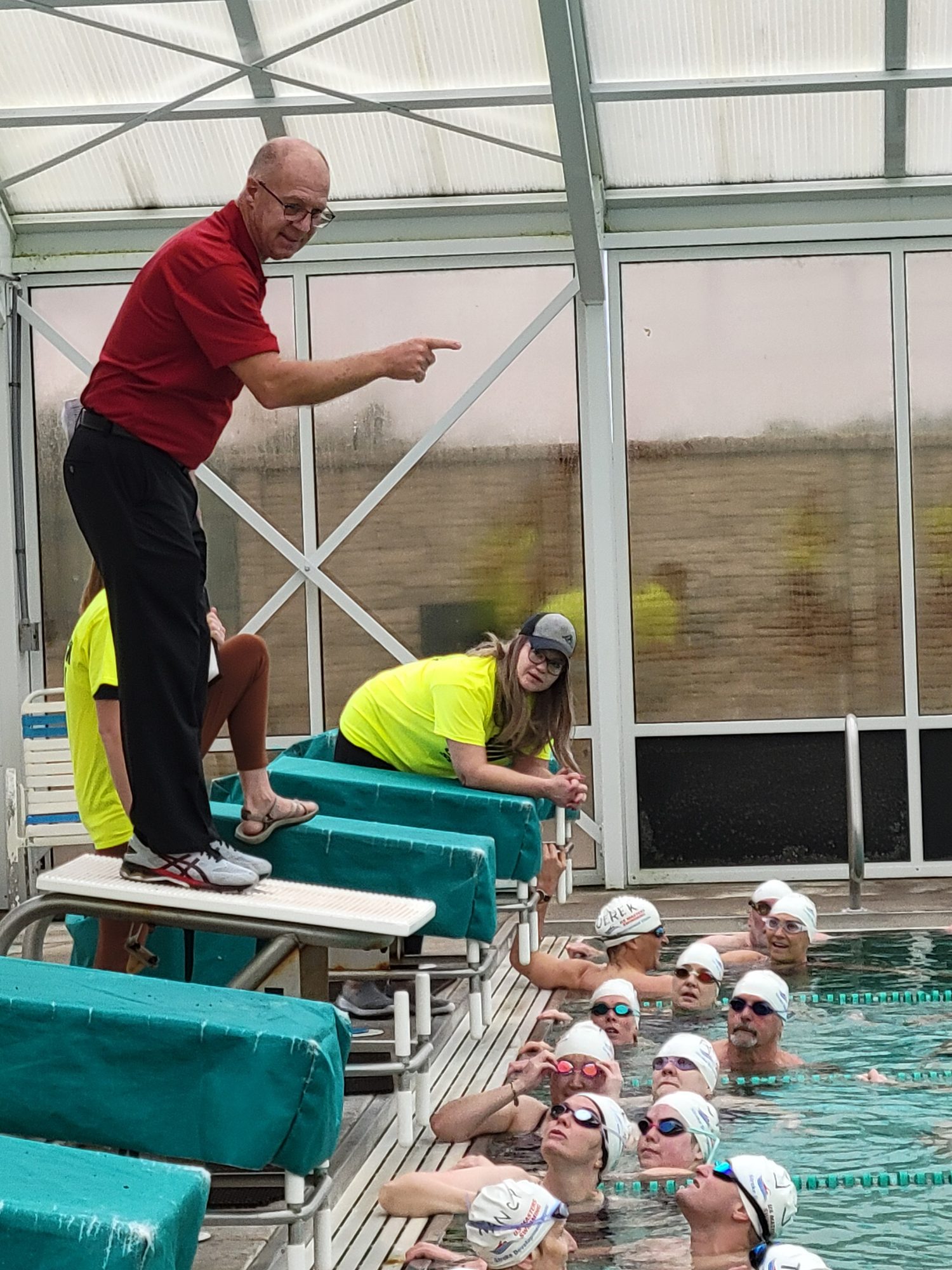 Bill Brenner on a starting block points out a detail to swimmers gathered at the wall
